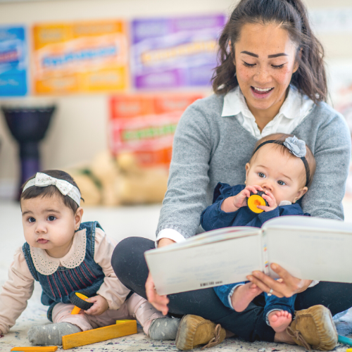 Woman sitting on the floor with two babies in her lap while reading to them
