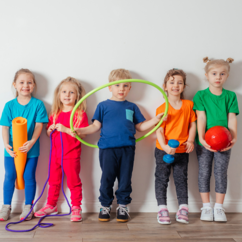 five children standing up against the wall holding different gym equipment