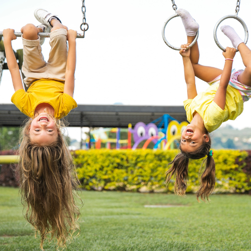 two young girls wearing yellow playing in a jungle gym hanging upside down